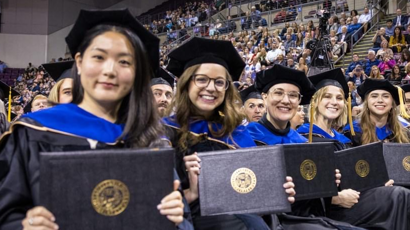 Psychology students at UCCS graduation holding degree covers.